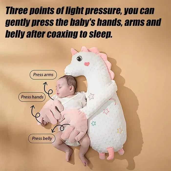 Pink plush unicorn sleep soother pillow with baby cuddled against the curved body.