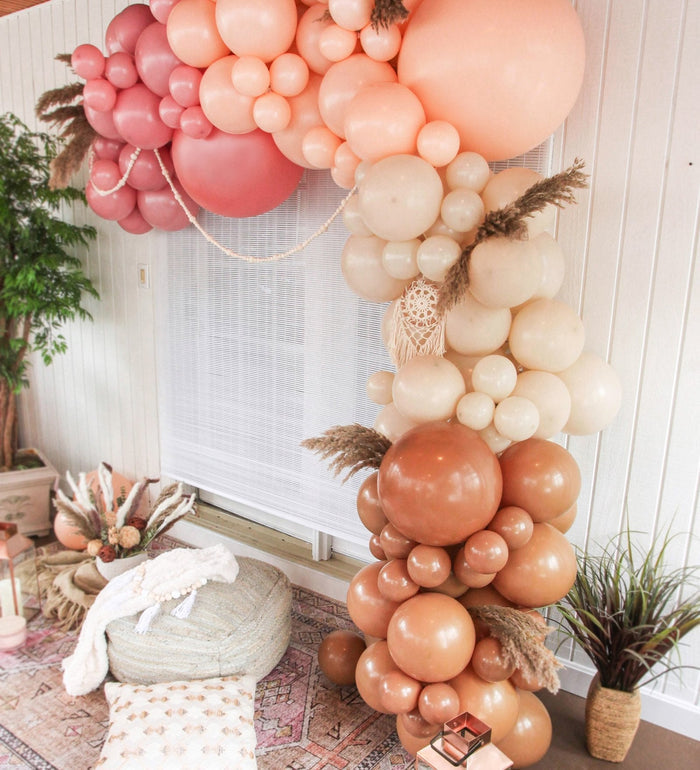 Balloon garland corner with blush, cream, and brown balloons stacked in layers