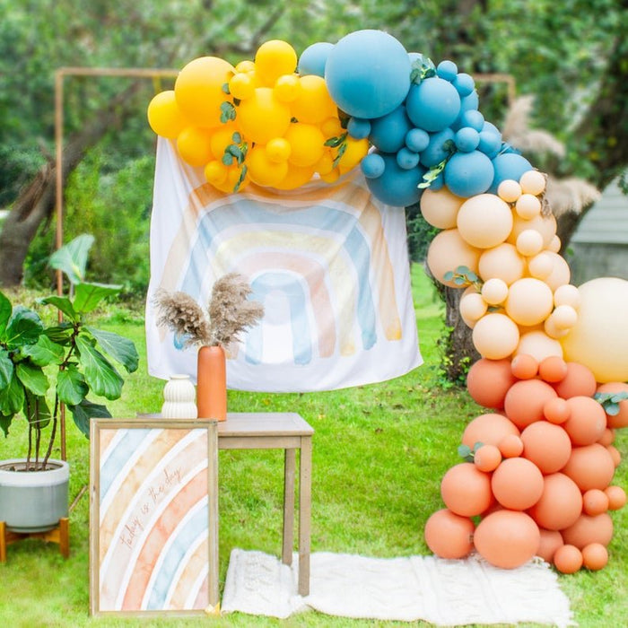 Pastel balloon garland arch with yellow, blue, and peach balloon clusters outdoors