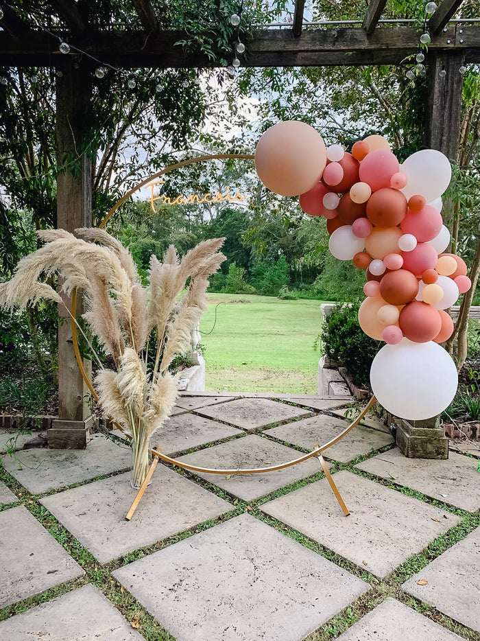 Outdoor balloon garland with peach, pink, and white balloons clustered along a frame