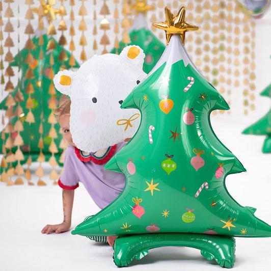 Green tree-shaped standing balloon with gold star topper, festive icons, and wide base.