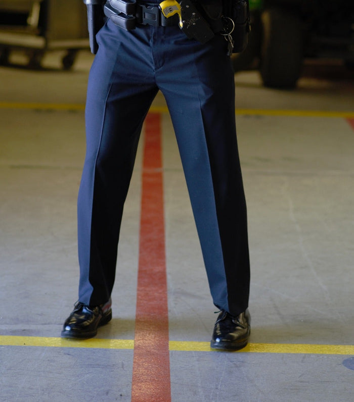 Photograph of a police officer's legs and feet in a dark garage with yellow and red lines on the floor the officer wears polished black shoes and a dark uniform with a visible utility belt