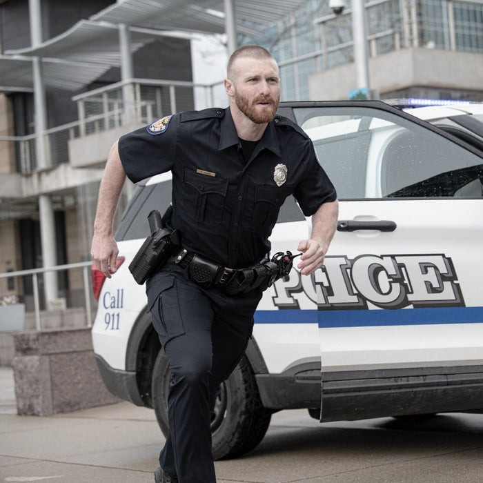 Photograph Police officer running towards a police car near modern buildings a black gun holster a police badge and a dark blue stripe on the car