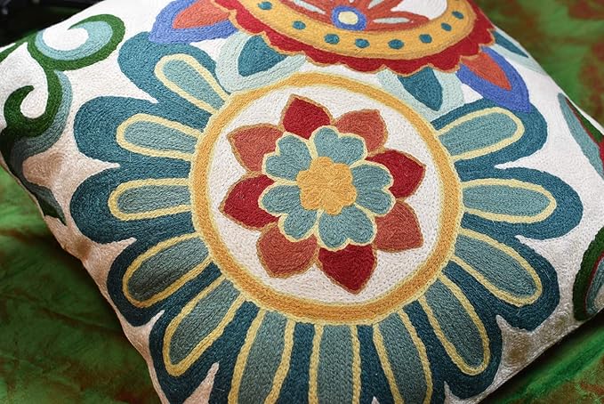 Close-up embroidered circular flower motif on cream fabric with teal and red thread details