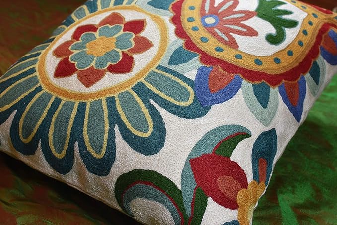 Embroidered floral pillow cover corner with blue-green petals and red flower accents on cream