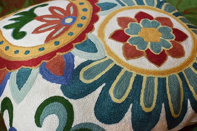 Close-up of two embroidered round flower designs on cream pillow cover with teal and red tones
