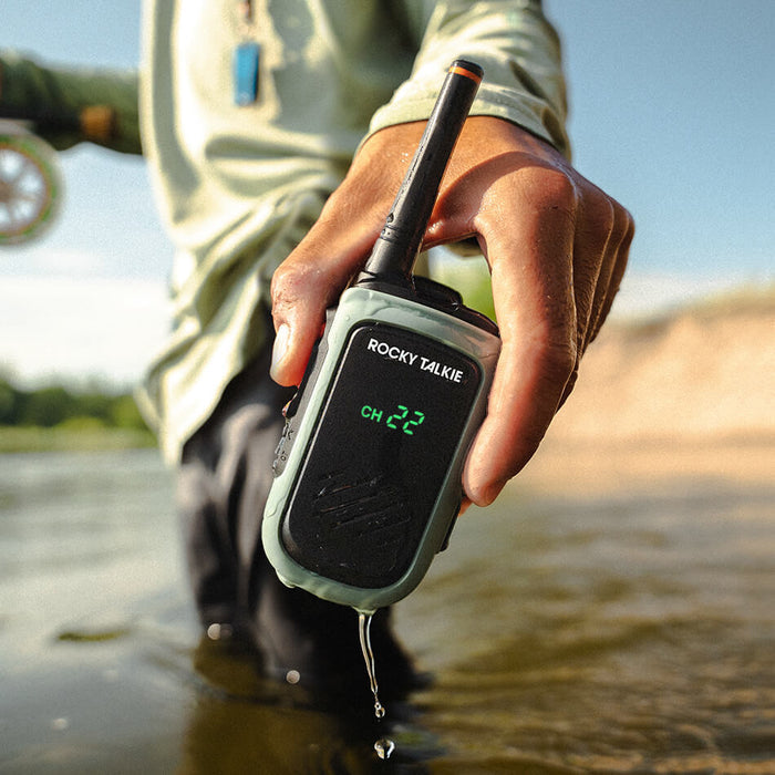 Hand holding Rocky Talkie 5 Watt Expedition Radio in Sage Green over a stream with water dripping off
