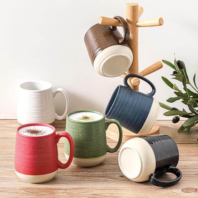 Ceramic coffee mug set with handles, mixed colors on wooden surface near olive plant