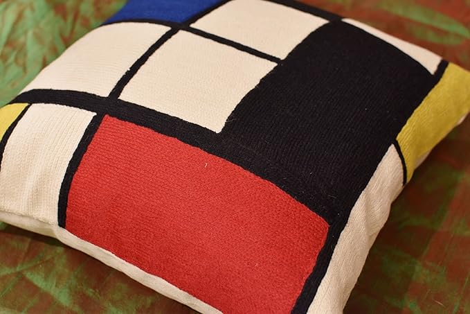Geometric pillow cover corner detail: red stripe, blue square, black grid on cream