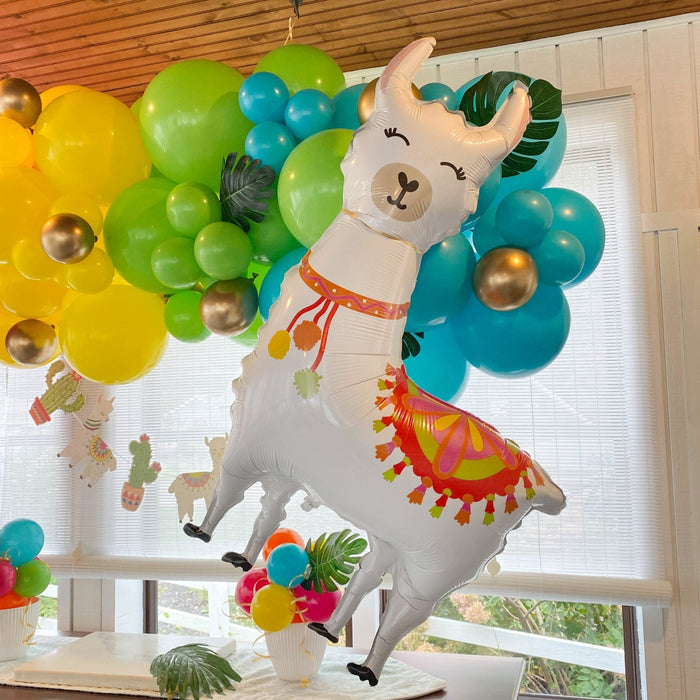 Llama-shaped balloon with white body, green leaf wings, and colorful skirt at party