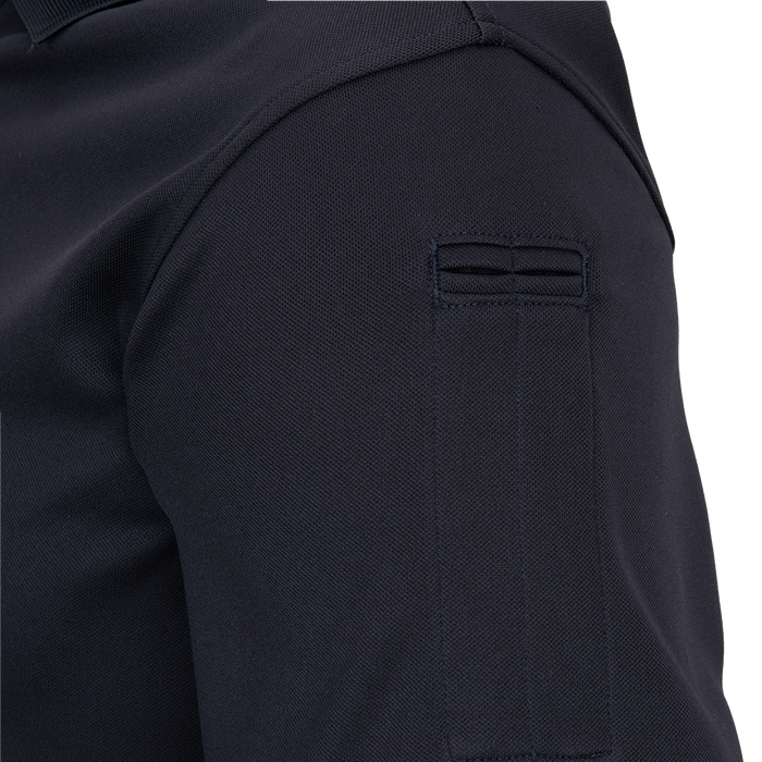 Close-up detail of a dark navy pique polo shirt showing a unique three-stitched pocket on the sleeve with subtle ribbed texture and a hint of collar