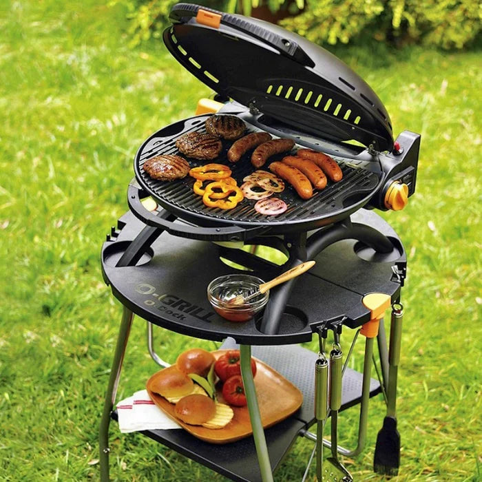 An o-dock holding up an o-grill being used to cook sausages and veggies