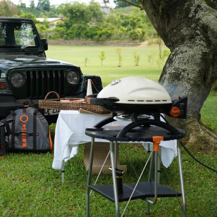 A cream O-Grill 900 held up on the O-Dock being used to cook at a campsite