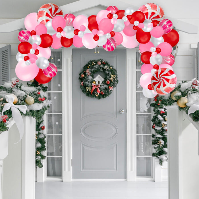 Red, pink, and white balloon garland draped across a front door with wreath