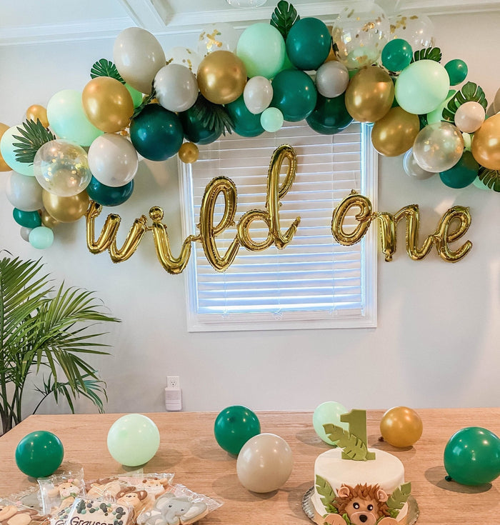 Latex balloon garland with gold, white, and green balloons above a birthday sign