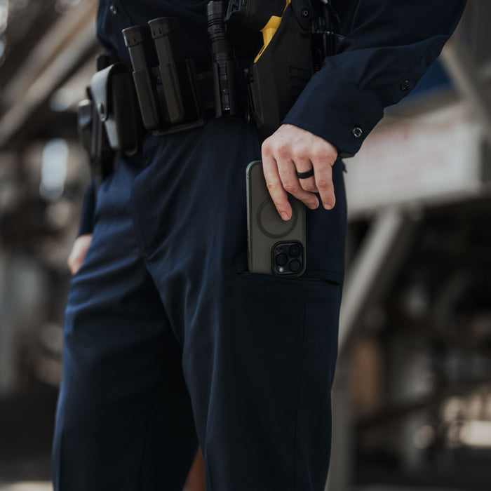 Photograph showing a police officer with a dark green phone in his pocket against a blurry industrial background featuring a yellow Taser and black tactical gear