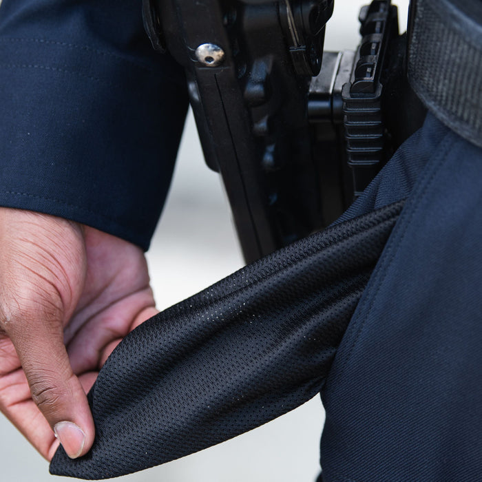 Photograph showing a close-up of a person's hand pulling out a black mesh pocket from dark blue pants with a black gun holster and silver screw visible