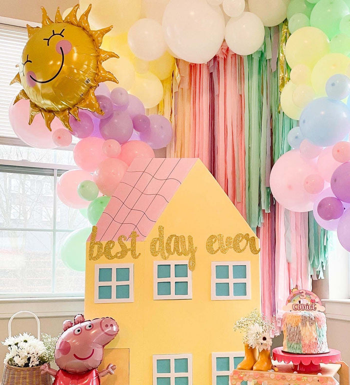 Smiling sun balloon above pastel balloons and a yellow house centerpiece