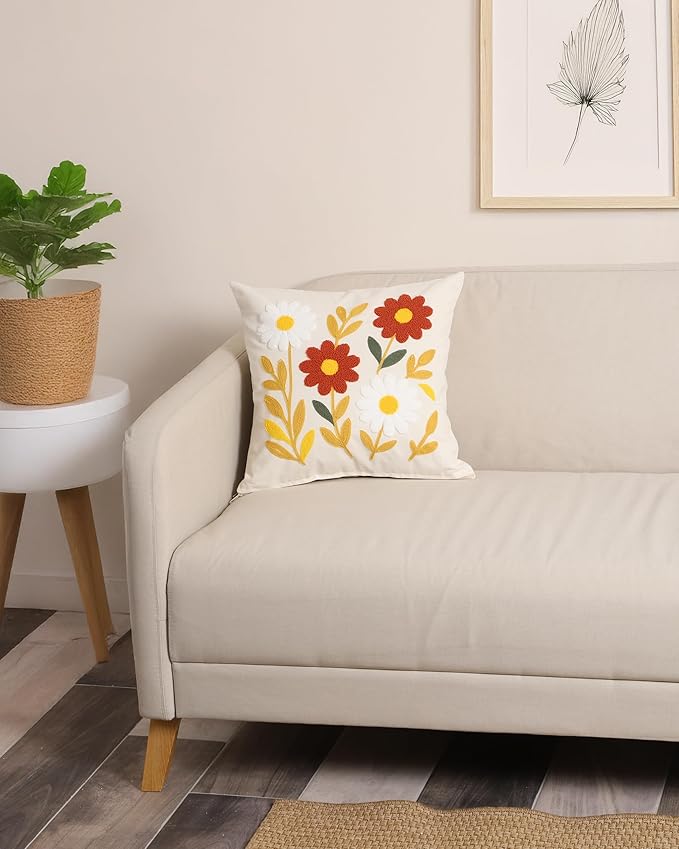 White pillow cover with embroidered daisies and red flowers on a sofa back