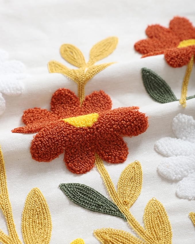 Close-up of white pillow cover with red flower, yellow stems, and green leaf embroidery