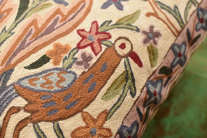 Cream pillow cover close-up with embroidered bird and vines in orange, blue, red